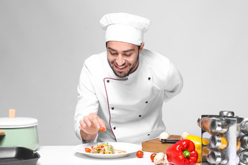 Young male chef cooking on light background