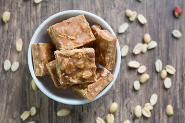 milk candy pieces with peanuts in white bowl with top view