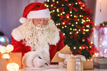 Authentic Santa Claus working at table in room decorated for Christmas