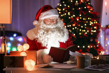 Fototapeta premium Authentic Santa Claus reading book at table in room decorated for Christmas
