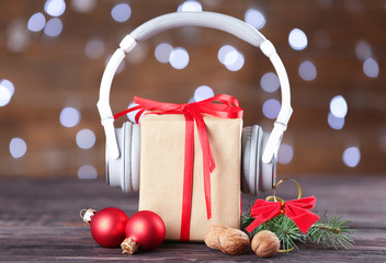 Beautiful composition with gift box and headphones on table against blurred lights. Christmas music...