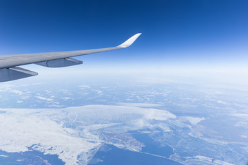 View of clear blue sky and airplane wing above snowy land in daylight.