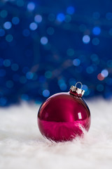 Burgundy Christmas ball on white fur with garland lights on blue bokeh background