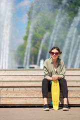 Portrait of happy young urban girl with skateboard in european city. Caucasian tourist background the big fountain