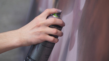 A hand with a spray can that draws a new graffiti on the wall. Photo of the process of drawing a graffiti on a wooden wall close-up. The concept of street art and illegal vandalism