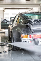 Man washing away the cleaning foam from a retro silver sports car in a car wash service
