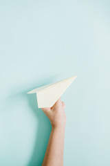 Obraz premium Women hand holding white paper plane on pale blue background. Flat lay, top view.