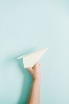 Fototapeta Women hand holding white paper plane on pale blue background. Flat lay, top view.