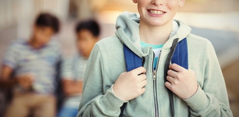 Smiling schoolboy standing with schoolbag in campus