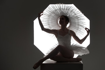 Silhouette of slim ballerina in tutu sitting on a cube against octabox in studio