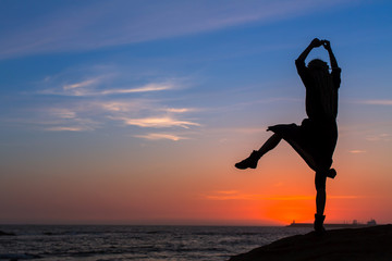 Silhouette of flexible girl on  sea coast during sunset.