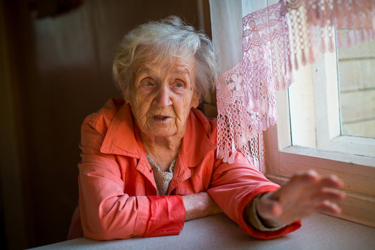 An elderly woman says gesturing with their hands sitting at table in the house.