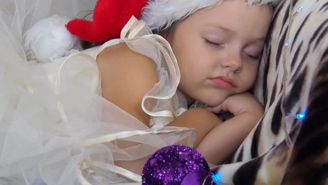 The child sleeps on the eve of Christmas. The little girl is sleeping in a Santa Claus hat.