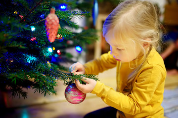 Adorable little girl decorating the Christmas tree with colorful glass baubles. Trimming the Christmas tree.