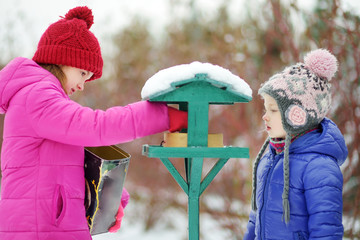 Two adorable sisters feeding birds on chilly winter day in city park. Children helping birds at...