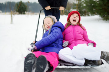 Two funny little sisters having a ride on a snow shovel on chilly winter day. Children playing in a snow during winter break.