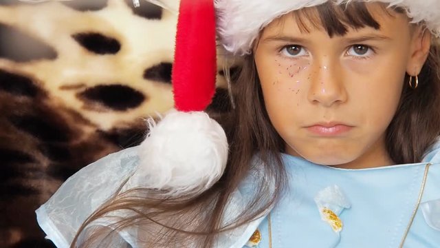 Emotion of a child in a santa claus hat. A crummy little girl in a Christmas hat.
