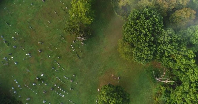 A straight down aerial view of a foggy Western Pennsylvania cemetery and wooded area on an early Autumn morning.  	