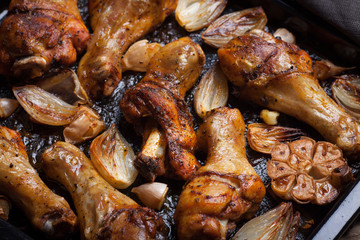 Oven-baked chicken leg quarters with onion, garlic and capsicum on a dark background closeup. Top view