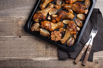 Oven baked chicken legs with onions, garlic and peppers on a dark wooden background closeup. Top view with copy space. Wooden rustic table