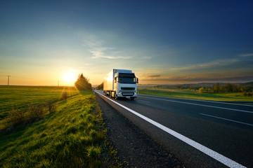 White truck driving on the asphalt road in rural landscape at sunset