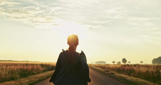 Happy Runner Woman Cheering on a Countryside Road at Sunrise. SLOW MOTION 4K DCi. Female jogger athlete training at dusk. Success and Achievement concept. Cinematic sports shot. 