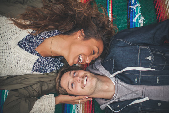 Young couple laying on colorful blanket and smiling.