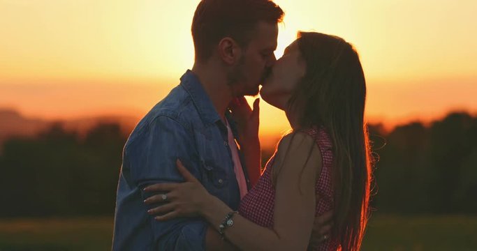 Young Couple Kissing at Sunset. SLOW MOTION 4K, Close Up. Romantic man and woman in love share a kiss. Love and affection. Cinematic backlit shot, Lens Flare.