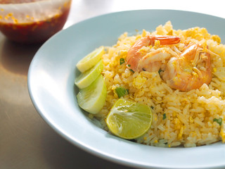 Thai local traditional street stall food: stir fried Jasmine rice with egg and shrimps, cucumber, lime, on blue plastic plate dish, with fish sauce spicy chili mix, on stainless steel table 