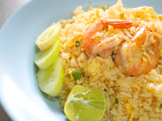 Close up of Thai local traditional street stall food: hot stir fried Jasmine rice with egg and shrimps, cucumber, lime, on blue plastic plate dish, perspective