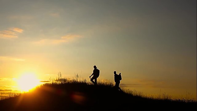 The Silhouette of two man standing on the top of mountain with Backpacks and other Gear expressing Energy and Happiness. Travel concept.