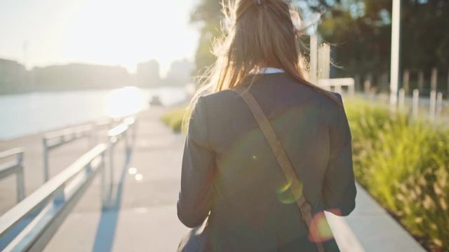 Young Businesswoman Using SmartPhone, Going to Work in the Sunny Morning City. SLOW MOTION. STEADICAM Stabilized Shot. Attractive Professional Business Woman with a cell phone in a city. Lens Flare. 