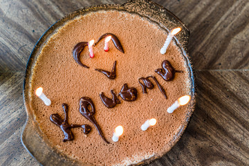 Flat top view of homemade tiramisu cake with lit birthday candles, heart and chocolate icing