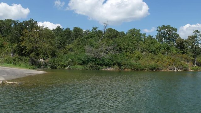 Wide shot of water from a lake flowing toward the shore, with green trees in the bank
