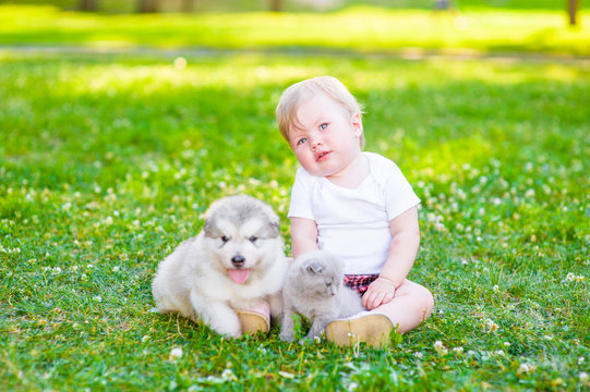 Baby Girl Sitting On The Grass With Puppy And Kitten In The Summer Park