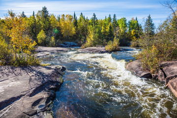 Fototapeta premium Old Pinawa Dam Provincial Heritage Park. Warm autumn day. Foam water rapids on the smooth stones of the Winnipeg River. The concept of ecological and adventure tourism
