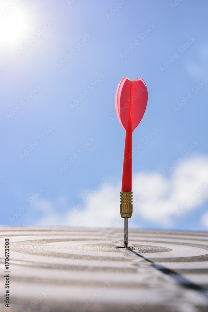 Aufkleber red dart arrow hitting in the target center of dartboard with blue sky background