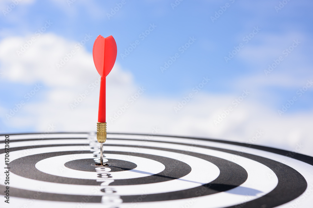 Poster red dart arrow hitting in the target center of dartboard with blue sky background