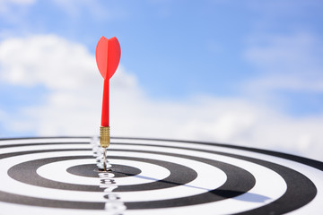 Red dart arrow hitting in the target center of dartboard with blue sky background