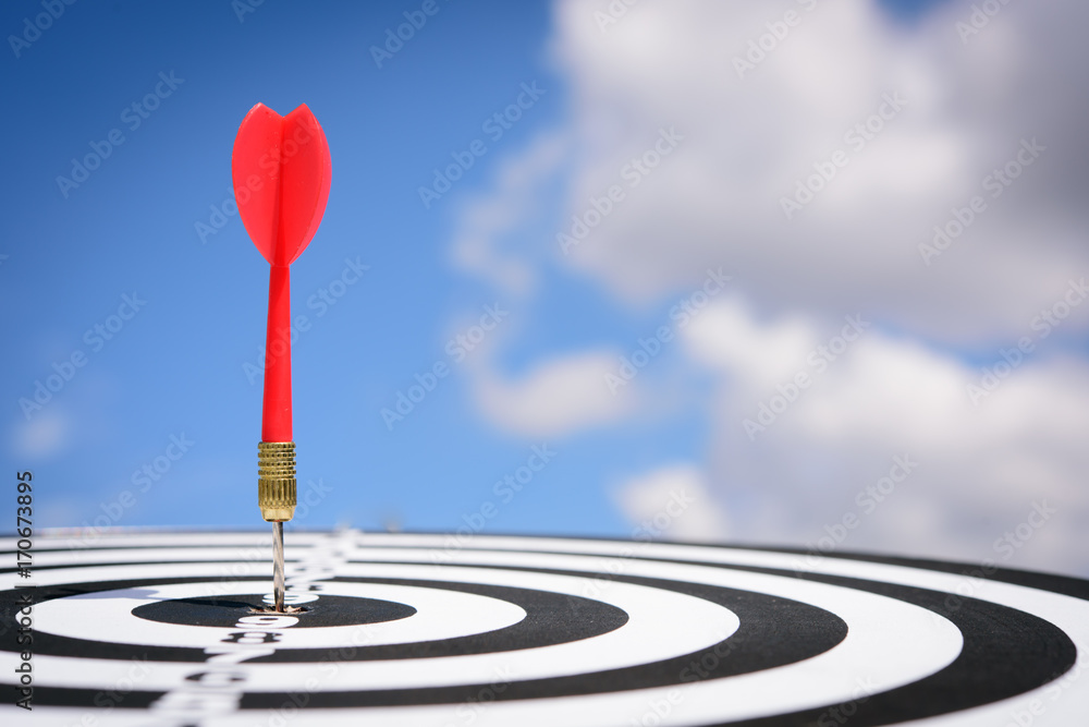 Poster red dart arrow hitting in the target center of dartboard with blue sky background