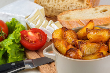 Breakfast from bread, cheese, tomatoes, potatoes and all-over salad on a wooden table closeup.