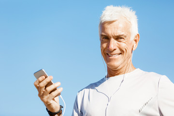 Male runner with his mobile smart phone standing outdoors