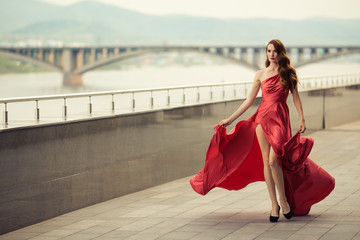 Beautiful woman in red fluttering dress. Urban background.