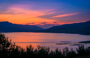 Landscape of a small bay surrounded by mountains during sunset with colorful sky and water reflection