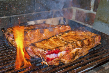 pork ribs marinated grilling on hot burning charcoal barbecue with some flames close-up