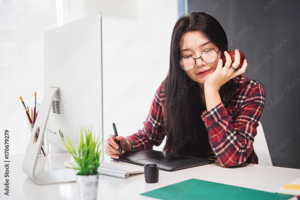 Poster young asian female designer using graphics tablet while working with computer at studio or office.