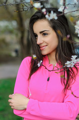 Naklejka premium Girl beautiful brunette. A sports body, having pumped up muscles. Bright colors, green, pink. Spring, trees in bloom. She does exercises.