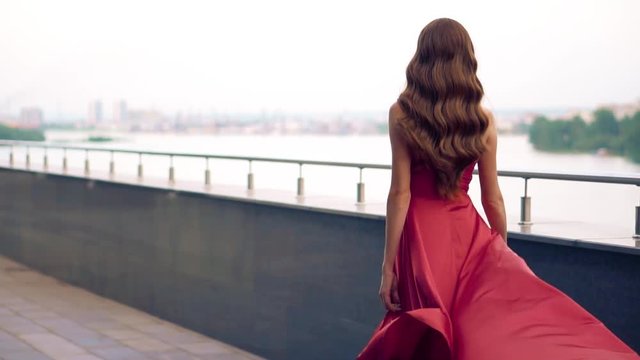 Beautiful woman in red fluttering dress. Urban background. Slow motion.