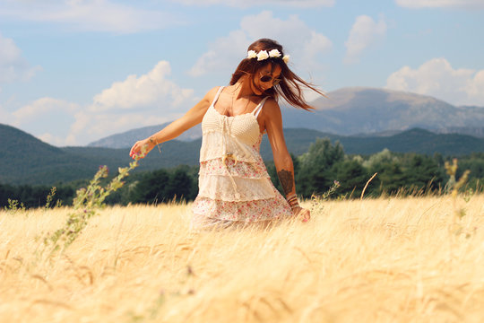 Beautiful woman with a boho style dancing in a wheat fields