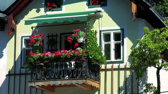 Detail of house and balcony with flowers in summer sunny day - woman sits on the balcony 